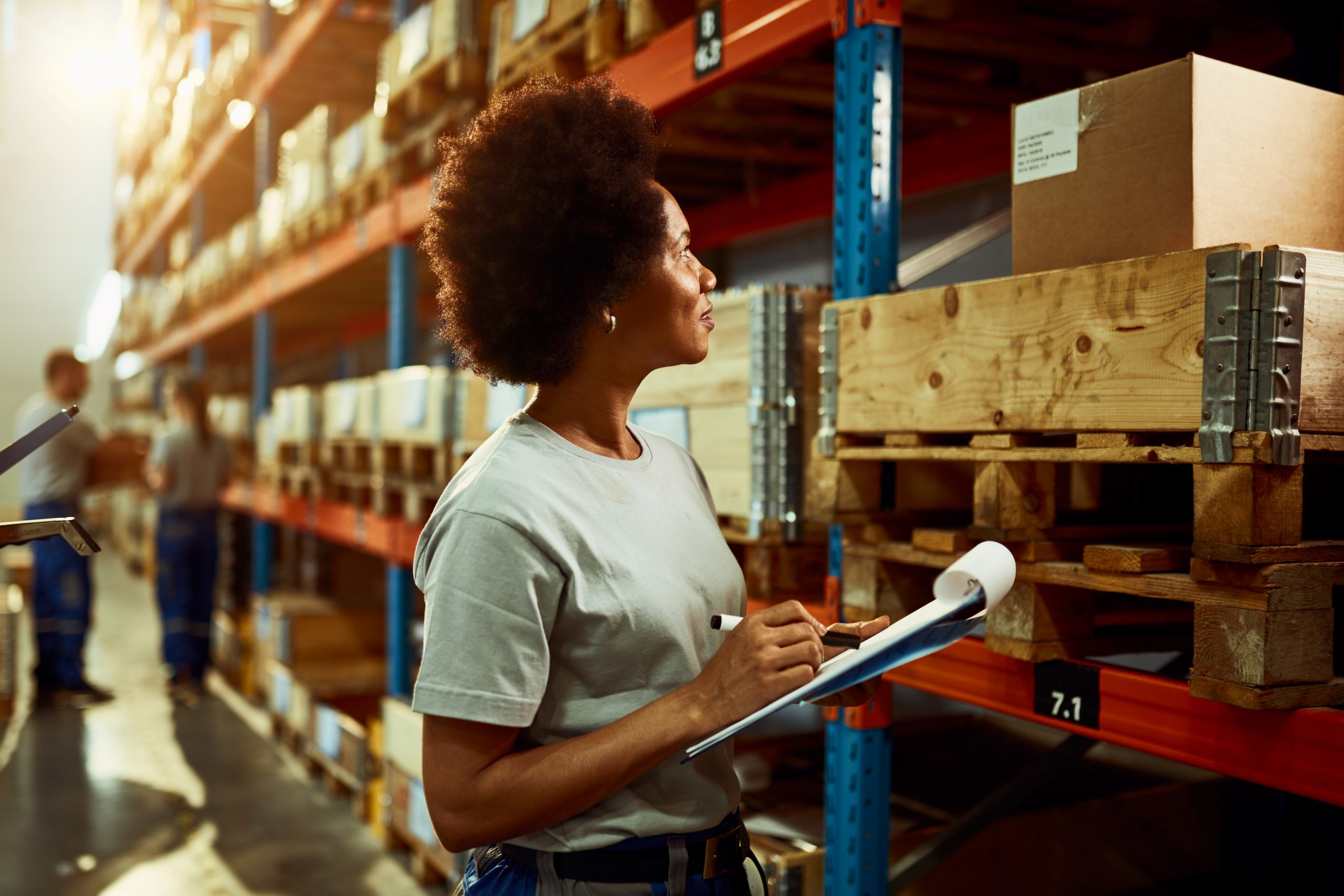 African American worker writing inventory list while checking stock in storage room.